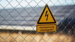 Warning sign indicating high voltage danger on a chain link fence near solar panels.