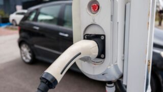 Close-up view of an electric car charging station with a plugged-in charger and cars in an urban environment.