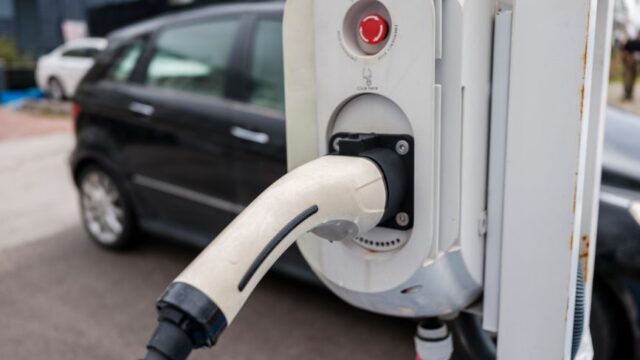 Close-up view of an electric car charging station with a plugged-in charger and cars in an urban environment.