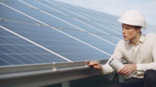 Focused young male employer in formal wear and hardhat working on solar panel station and checking details of modules