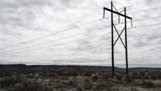 High voltage power lines stretch across a dramatic, cloudy sky landscape, embodying industrial beauty.