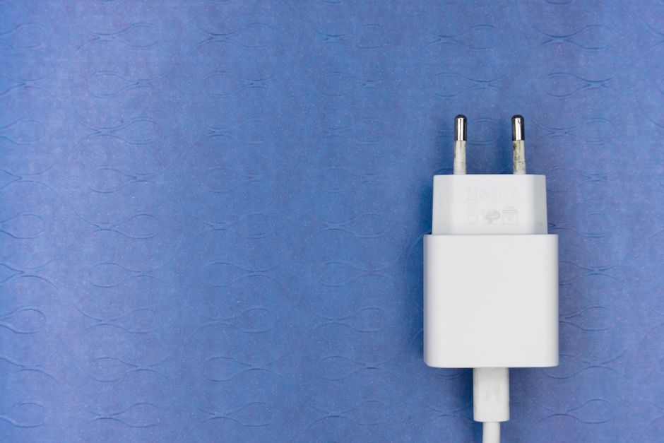 White electric charger plug on a blue textured surface, ideal for tech visuals.