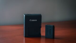 Close-up of a Canon battery and charger on a wooden table with a blurred background.