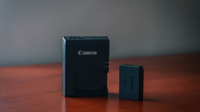 Close-up of a Canon battery and charger on a wooden table with a blurred background.