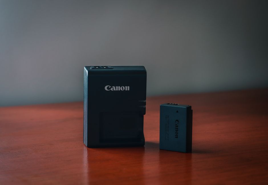 Close-up of a Canon battery and charger on a wooden table with a blurred background.