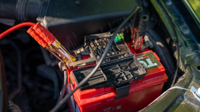 Close-up view of a car battery with red jumper cables connected, outdoors.