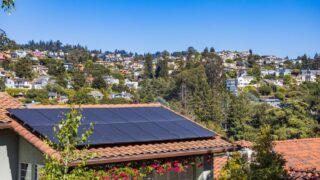 Solar panels on a suburban home, surrounded by lush greenery and a sunny blue sky.