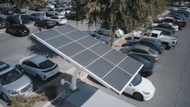 Electric cars charging at a solar-powered station in a parking lot.