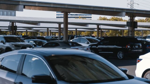 A busy outdoor parking lot filled with various parked cars under solar panel structures.