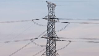 High voltage power transmission tower under a clear blue sky, symbolizing energy infrastructure.