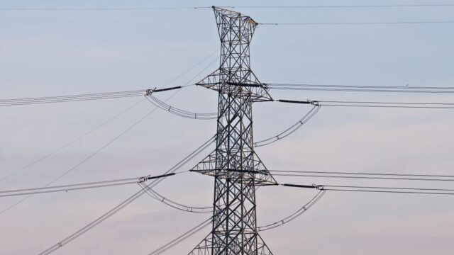 High voltage power transmission tower under a clear blue sky, symbolizing energy infrastructure.