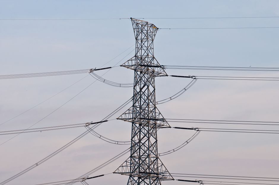 High voltage power transmission tower under a clear blue sky, symbolizing energy infrastructure.