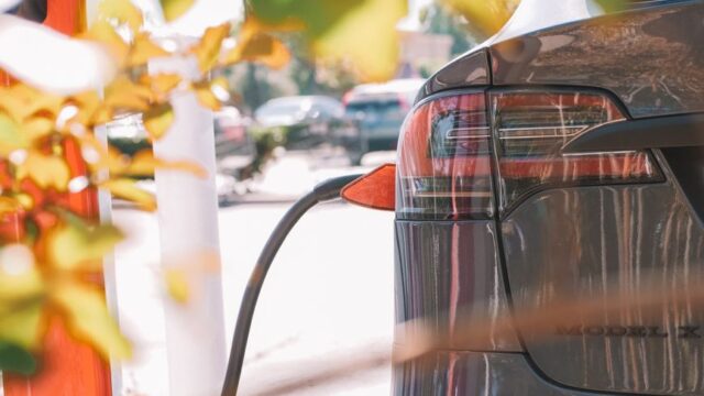 Close-up of an electric car connected to a charging station outdoors in sunlight.
