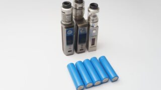 Three vape mods and six blue 18650 batteries on a white surface.