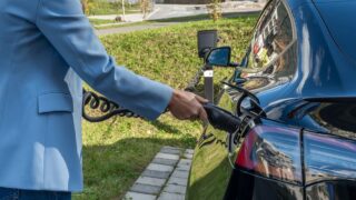 Person connecting an electric car to a charging station outdoors, showcasing green energy transition.