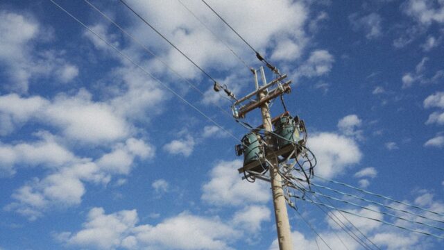 High voltage power lines stretching against a cloud-dappled blue sky, showcasing modern energy infrastructure.