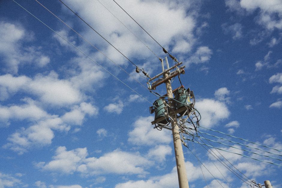 High voltage power lines stretching against a cloud-dappled blue sky, showcasing modern energy infrastructure.