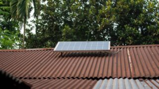Solar panel on a rusty corrugated roof with green foliage background, symbolizing sustainable energy.