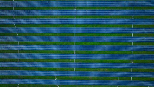 Aerial photograph of a solar farm featuring rows of solar panels and green spaces.