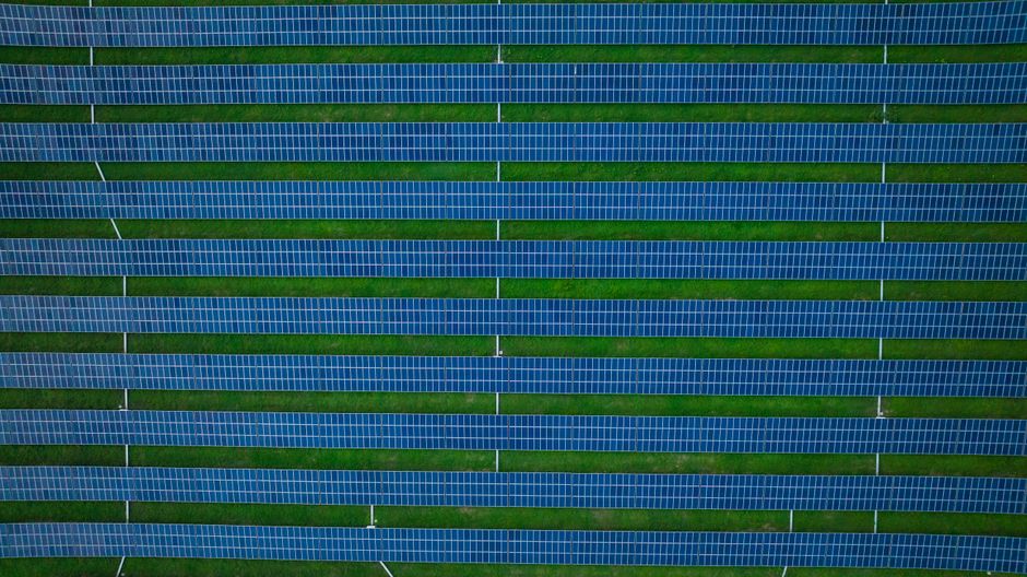 Aerial photograph of a solar farm featuring rows of solar panels and green spaces.