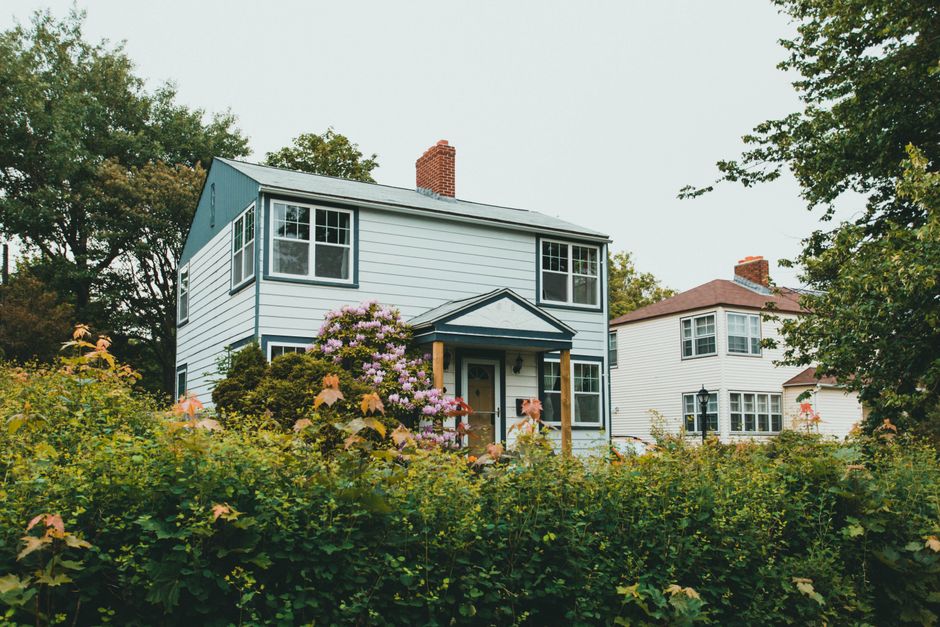 Charming two-story wooden house surrounded by lush greenery and vibrant flowers in a suburban neighborhood.