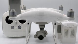 A white drone alongside its controller and batteries, showcasing modern technology on a white background.