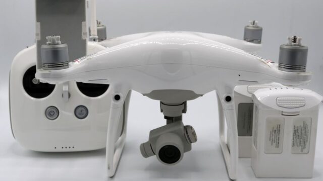A white drone alongside its controller and batteries, showcasing modern technology on a white background.