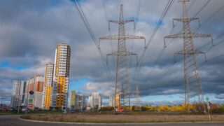 Urban landscape featuring high voltage power lines and modern buildings under a cloudy sky.
