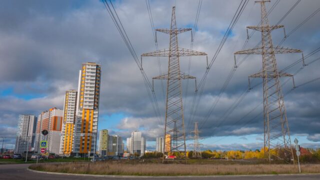 Urban landscape featuring high voltage power lines and modern buildings under a cloudy sky.