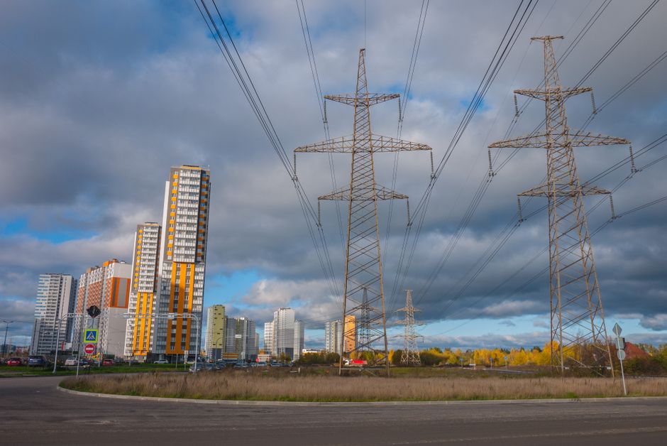 Urban landscape featuring high voltage power lines and modern buildings under a cloudy sky.