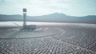 Wide aerial shot of a vast solar power station with mountain backdrop.