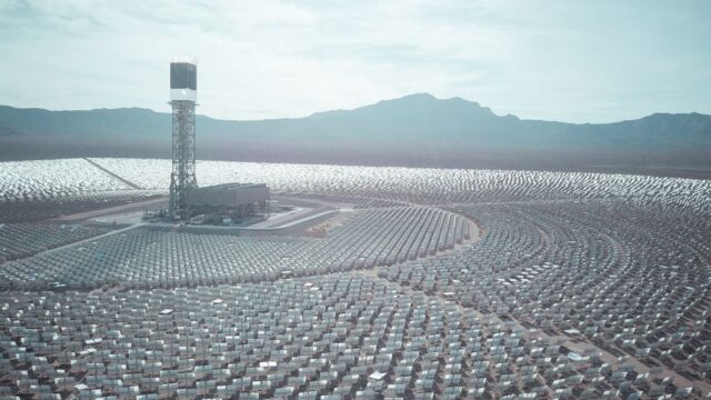 Wide aerial shot of a vast solar power station with mountain backdrop.