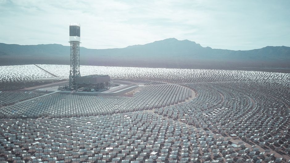 Wide aerial shot of a vast solar power station with mountain backdrop.