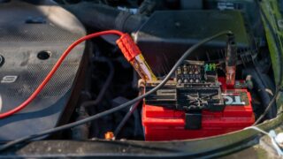 Close-up of a car battery with attached jumper cables in an engine bay.