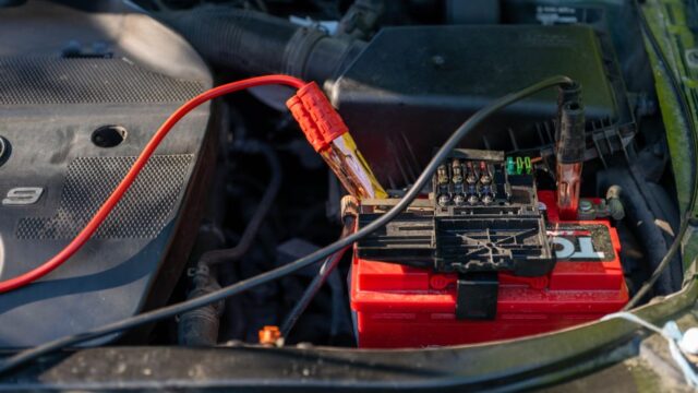 Close-up of a car battery with attached jumper cables in an engine bay.
