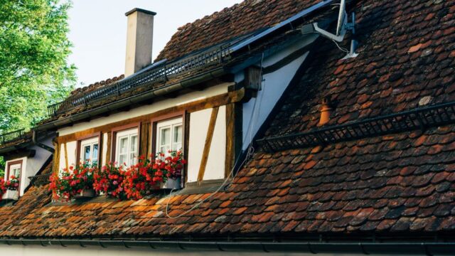Close-up of a quaint house with a red brick roof, solar panels, and flower boxes.
