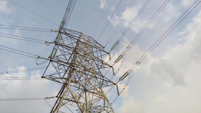 A close-up view of a high voltage transmission tower and lines against a cloudy sky.