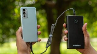 Close-up of hands holding a smartphone connected to a power bank outdoors.