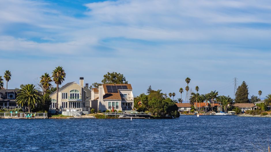 Charming waterfront homes with palm trees and solar panels reflecting in blue water.