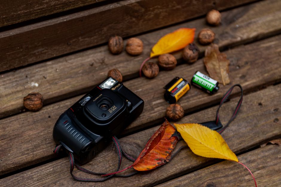 An artistic flat lay of a vintage camera with autumn leaves and batteries.