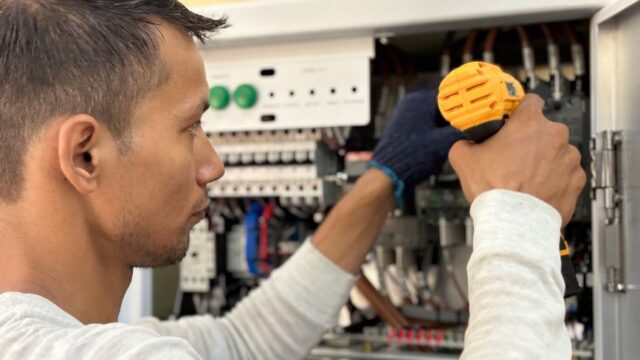 Focused technician using a drill on an electrical panel, showcasing expert workmanship.