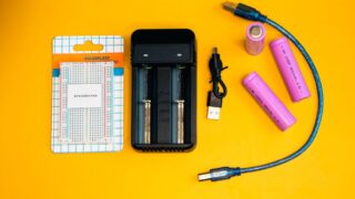 Flat lay of electronics including a breadboard and battery charger against a vibrant yellow backdrop.