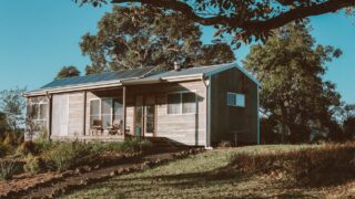 A charming wooden house in Australia featuring solar panels, surrounded by lush greenery.