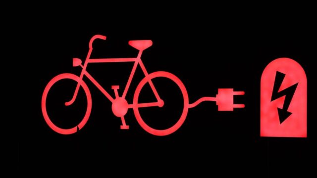 Glowing red outline of an electric bicycle and charging plug on a black background.