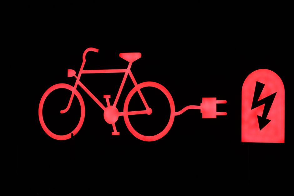 Glowing red outline of an electric bicycle and charging plug on a black background.