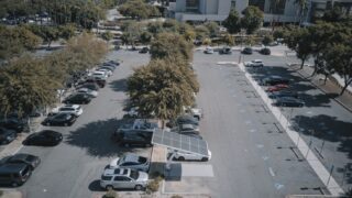 High-angle view of a parking lot with solar panels and parked vehicles, surrounded by greenery.