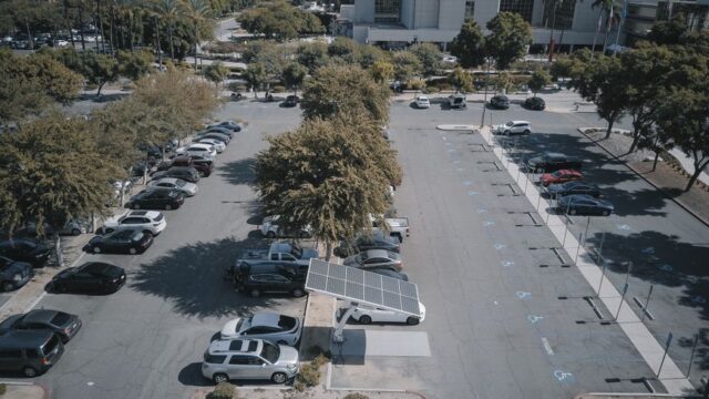 High-angle view of a parking lot with solar panels and parked vehicles, surrounded by greenery.