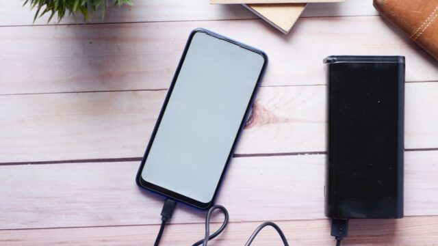 Smartphone charging with a power bank on a wooden desk, showcasing modern technology essentials.