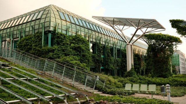 Eco-friendly building with rooftop gardens and solar panels in an urban setting, captured in daylight.