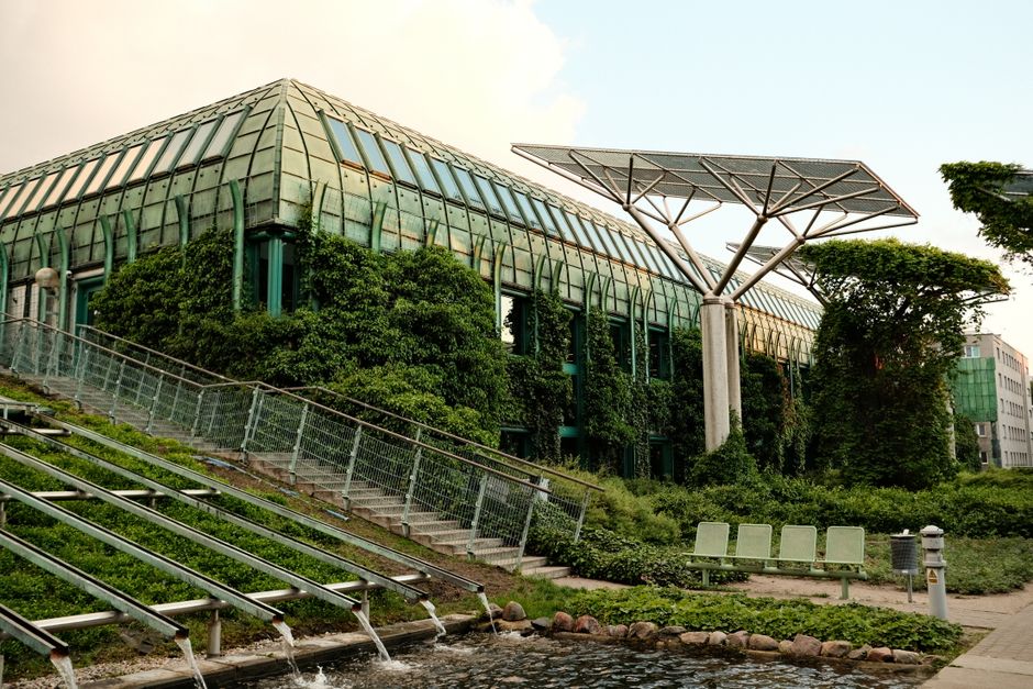 Eco-friendly building with rooftop gardens and solar panels in an urban setting, captured in daylight.